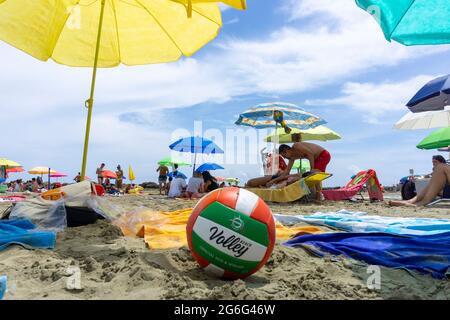 Palla da pallavolo rossa, verde e bianca sulla spiaggia circondata da asciugamani Foto Stock