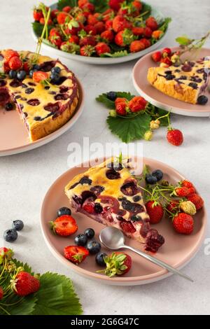 Pezzo di torta al mirtillo di fragola con frutti di bosco freschi in un piatto rosa su sfondo grigio Foto Stock
