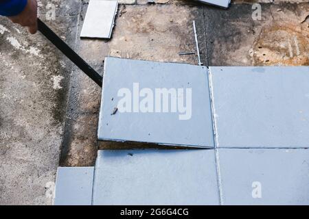 piastrelle blu per esterni che si strappano fino a rivelare pavimentazione in calcestruzzo sotto, concetto di demolizione o ristrutturazione e miglioramento della casa Foto Stock