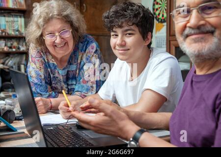 Nonni e Teenage Boy a casa si sono riuniti intorno laptop sorridendo Foto Stock