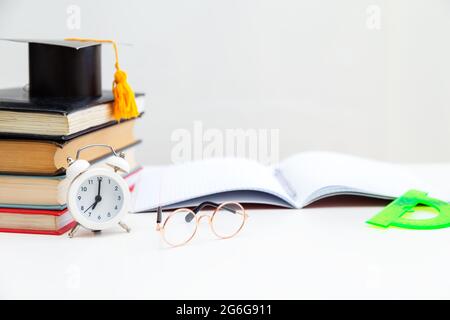 Libri, materiali per la scrittura, occhiali, notebook e sveglia sul desktop. Ritorno a scuola. Concetto di apprendimento e autoistruzione. Foto Stock