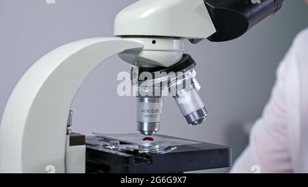 Il dipendente donna concentrato con bicchieri preleva la goccia di sangue dalla provetta con una pipetta lunga vicino al microscopio e lavora in vista ravvicinata dell'ospedale Foto Stock