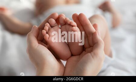 Primo piano dei piccoli piedi del neonato nelle mani della mamma Foto Stock