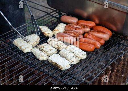 Avere un barbecue con i carboni caldi all'aperto, cuttando il formaggio haloumi con le pinze su un barbecue o barbecue. Foto Stock