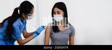 Donna asiatica medico che tiene la siringa e che usa il cotone prima di fare l'iniezione alla gente del paziente in maschera medica. Vaccino Covid-19 o coronavirus Foto Stock