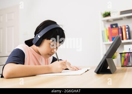 Tailandese Asian ragazza studente di apprendimento on-line su tablet a casa, bambino giovane studiare e lavorare felicemente durante il blocco a causa di covid 19 o coronavirus Foto Stock