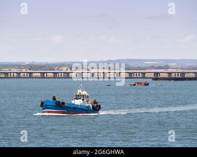 La barca da pesca va in mare con il molo del porto sullo sfondo Foto Stock