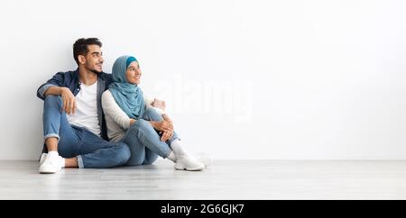 Donna felice in hijab seduta sul pavimento con suo marito Foto Stock