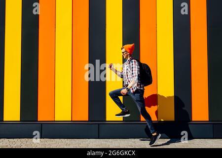 Foto di allegro positivo emozionante corsa saltando hipster uomo con valigetta cercando di successo contro isolato urbano multicolore muro sfondo Foto Stock