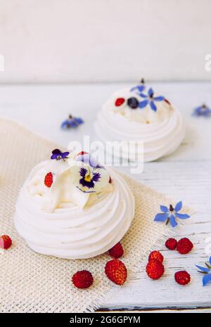 Piccoli dolci di meringa, decorati con panna montata, bacche fresche e fiori commestibili reali. Foto Stock
