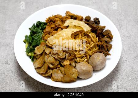 Delizioso e gustoso Mie ayam o Mie Yamin o Yamin Noodle con carne di pollo, verdure, Pangsit Goreng, Pangsit Rebus e polpette su piatto bianco Foto Stock