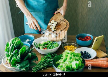 Una donna inriconoscibile chef prepara un'insalata e mette gli ingredienti in un grande recipiente. Il concetto di mangiare sano e cucinare a casa. Foto Stock