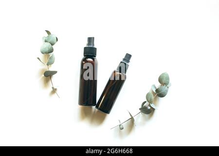 Bottiglie cosmetiche in vetro ambrato scuro su sfondo bianco con ramoscelli di eucalipto verde. Primo piano, spazio per la copia. Blog di bellezza, il concetto di trattamento salone, il layout della confezione del marchio in stile minimalismo Foto Stock