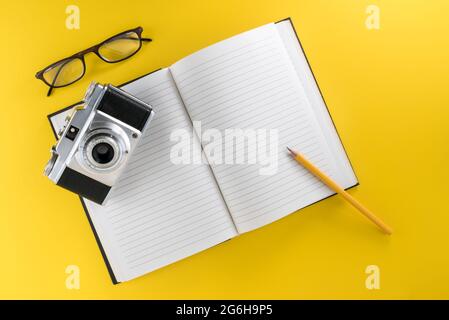 Fotocamera retrò su notebook con linee nere su sfondo giallo con matita gialla e occhiali, concetto di viaggio, spazio di copia Foto Stock