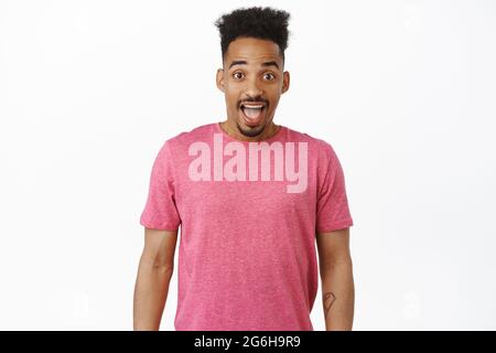 Immagine di un giovane afro-americano eccitato e sorpreso, che guarda entusiasta e divertito, che guarda le grandi notizie, sorridente stupito, in piedi in rosa t. Foto Stock
