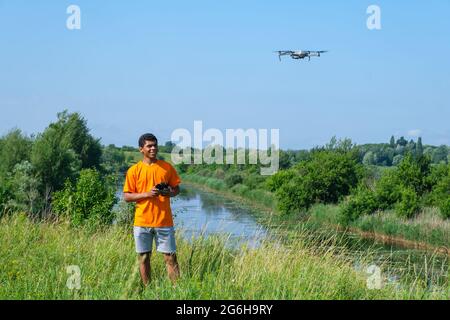 Uomo afroamericano che opera con il drone con il controller in mani sul prato Foto Stock