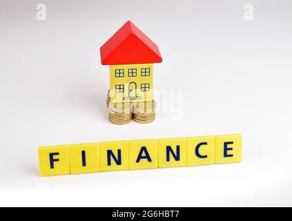 Una casa giocattolo seduta su una pila di monete con la parola 'Finanza' davanti ad essa. Foto Stock