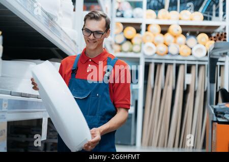 venditore con un rotolo di isolante in mano in piedi in un negozio di hardware. Foto Stock