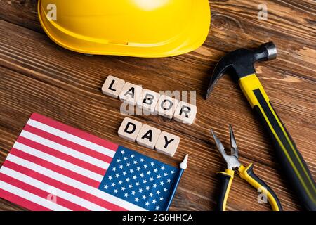 bandiera usa, martello, pinze, cappello e cubetti con scritta labor day su tavolo di legno Foto Stock