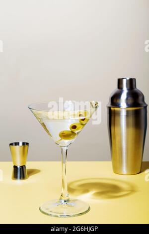 Bicchiere di cocktail martini con olive verdi. Nelle vicinanze, jigger e shaker. Mettere a fuoco le ombre Foto Stock
