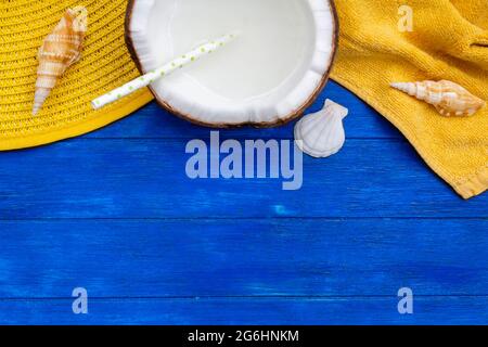 Vista dall'alto del cappello estivo, telo da spiaggia, conchiglie e cocco con paglia su tavolo di legno blu con spazio per la copia Foto Stock