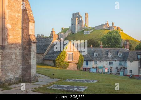 Corfe Castle, UK - Giugno 23 2021: Rovine del castello medievale in cima a una collina nel pittoresco e storico villaggio di Corfe Castle, Dorset, Inghilterra con il sole dell'ora d'oro Foto Stock