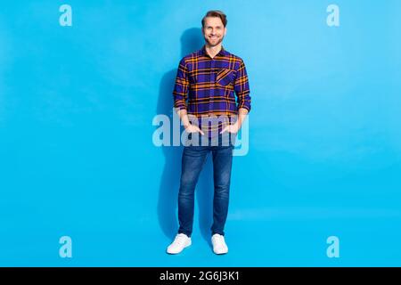 Ritratto di dimensioni complete di un uomo soddisfatto e amichevole in piedi mettere le mani in tasche isolate su sfondo blu Foto Stock