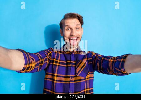 Foto di carino adorabile giovane gentiluomo vestito a scacchi tacking selfie mostrando lingua isolato sfondo di colore blu Foto Stock