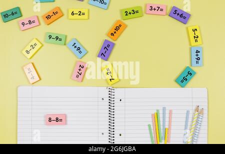 Apri notebook, matite ed esempi matematici su sfondo giallo. Torna a scuola, divertente imparare a contare per i bambini. Foto Stock