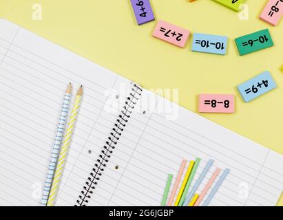 Apri notebook, matite ed esempi matematici su sfondo giallo. Torna a scuola, divertente imparare a contare per i bambini. Foto Stock