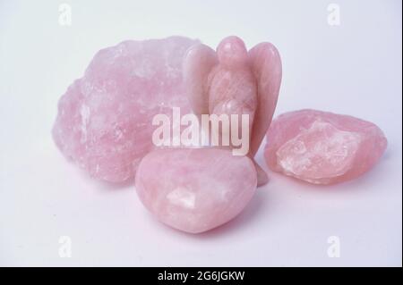 Pietra di quarzo rosa in forme diverse, pietra ruvida, angelo o anche cuore su sfondo bianco Foto Stock