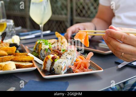 uomo che mangia sashimi di salmone in ristorante giapponese. Uomo che tiene i chopsticks che mangia sashimi di salmone fresco Foto Stock