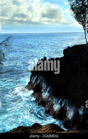 Pescatore locale perches sulle rocce per una notte di pesca. È seduto sul bordo di una sporgenza rocciosa al McKinzie state Park sulla Big Island of H. Foto Stock