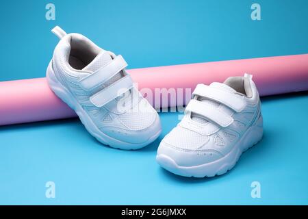 primo piano due scarpe sportive bianche da donna su un tubo di carta rosa lungo su uno sfondo blu geometrico in uno stile alla moda Foto Stock