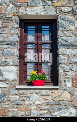 Finestra con persiane in legno decorate con fiori in fiore in una pentola. Casa tradizionale in pietra ad Afissos, sulle pendici del monte Pelion, in Gr Foto Stock