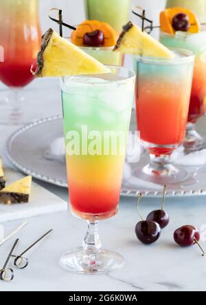 Primo piano di una coda di mocktail fruttata e gelata guarnita con un cuneo di ananas con altre code di mocktail dietro. Foto Stock