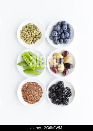 Vista dall'alto delle piccole ciotole piene di vari ingredienti sani e crudi, su sfondo bianco. Foto Stock