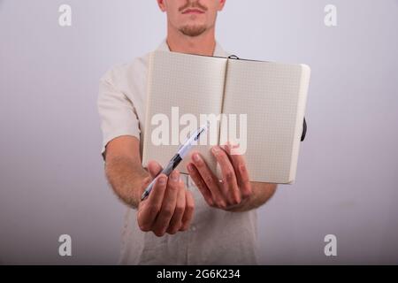 Primo piano di un'agenda vuota aperta e di una penna tenuta da un uomo sul retro fuori fuoco. Foto Stock