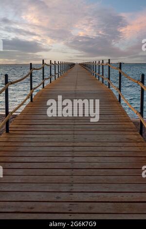 Molo di legno che si estende nel mare per i turisti all'alba. Foto Stock