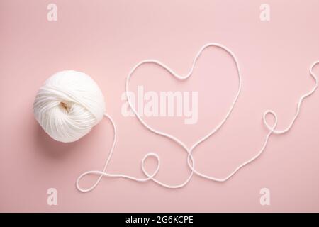 Aghi bianchi in lana e maglia su sfondo rosa pastello. Lavorazione a maglia hobby. Vista dall'alto - immagine Foto Stock