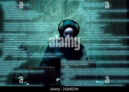 Anonimo hacker indossare maschera viso lavorare sul computer in camera oscura Foto Stock