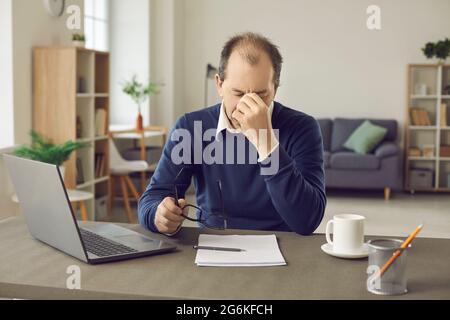 L'uomo d'affari anziano stanco del carico di lavoro soffre di mal di testa e mancanza di sonno. Foto Stock