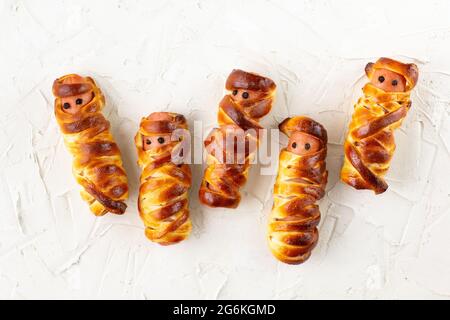 Spaventose mummie di salsiccia in pasta per la festa dei bambini. Divertente pazzo Halloween cibo per i bambini su sfondo bianco Foto Stock