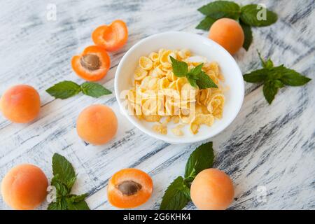 Fiocchi di mais con albicocca al tavolo di legno bianco. Colazione estiva sana, composta da diversi ingredienti gialli, fiocchi di mais frullati Foto Stock
