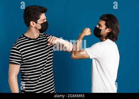 Bruna bianca due uomini in maschera viso gomito che urla isolato su sfondo blu Foto Stock