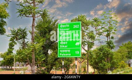 07 luglio 2021 - Reengus, Sikar, India. Segnaletica stradale con distanze dalle principali città lucidate e sfondo cielo nuvoloso. Cartello stradale con sfondo verde Foto Stock