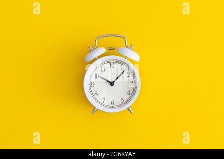 Orologio bianco antico su sfondo giallo. Composizione di posa piatta. Vista dall'alto. Foto Stock