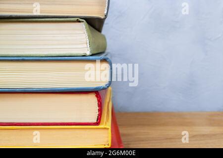 Pila di libri hardback colorati su tavola di legno vicino contro parete di cemento grigio e blu Foto Stock