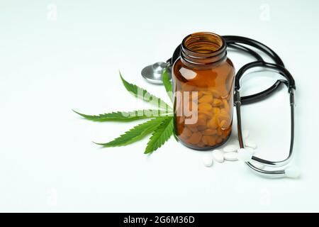 Flacone con pillole, foglia di cannabis e stetoscopio su sfondo bianco Foto Stock