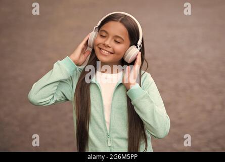 ragazza allegra indossare auricolari con musica canzone all'aperto godendo di melodia, scuola di formazione online Foto Stock